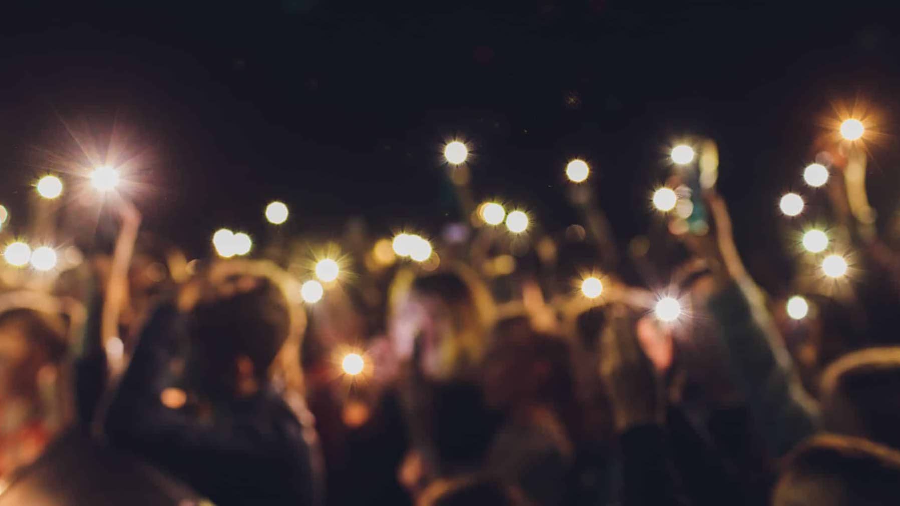 People standing with arms raised shoot a video on the phone at a street music show, blurred background