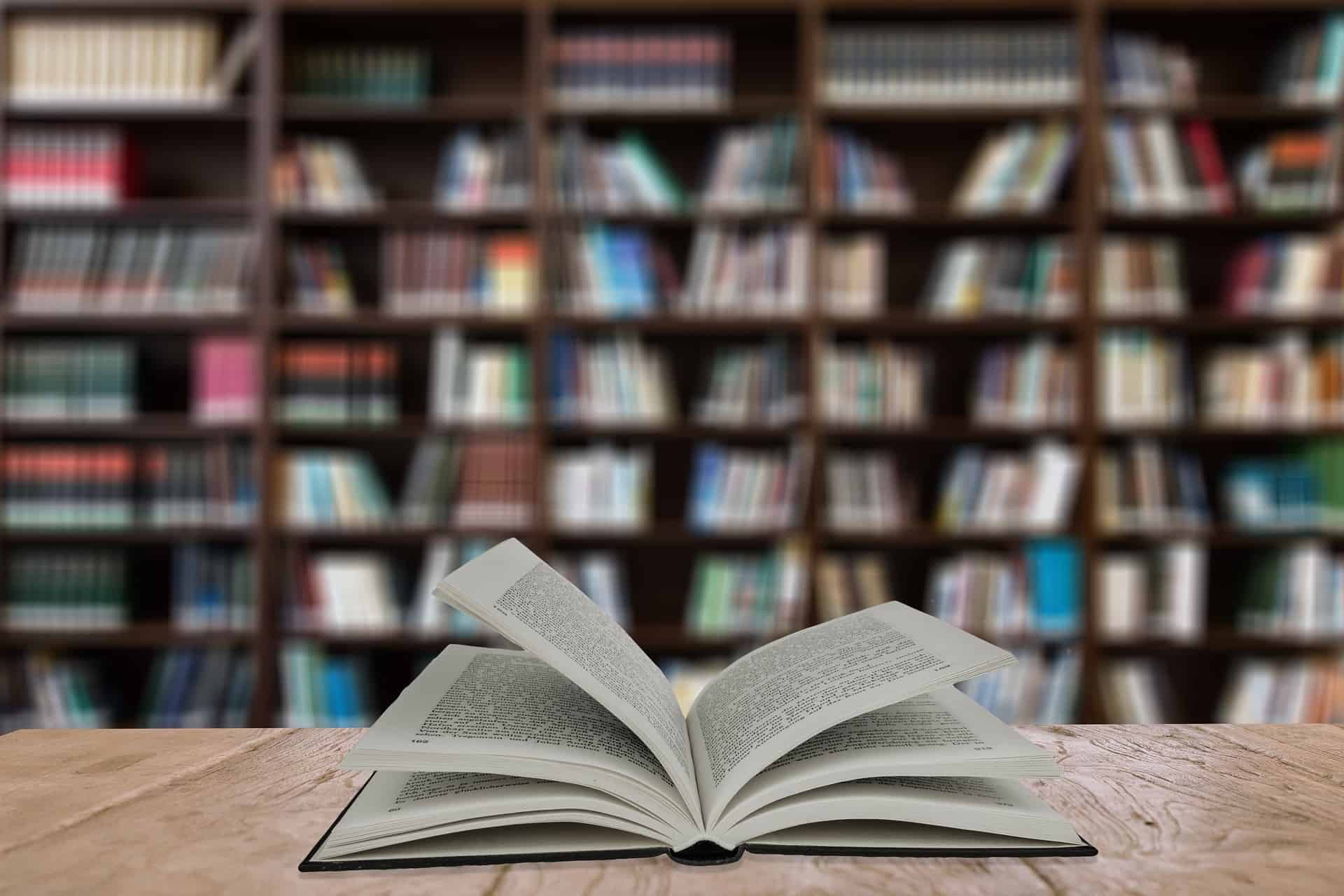 book with open pages laying on a table in front of a large book shelf